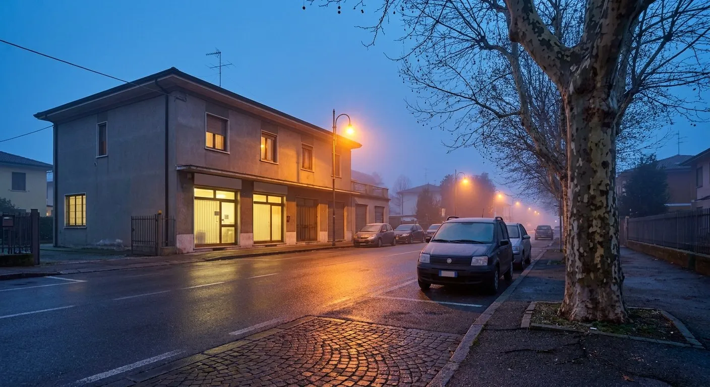 Una strada di periferia all'alba, con le luci accese di un locale al piano terra